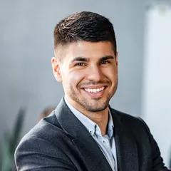 Smiling man with short dark hair in a grey blazer and light blue shirt
