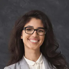 Smiling woman with long dark hair wearing black glasses and a grey blazer